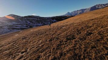 Aerial view of a man in sportswear running fast across fields. A guy exercising outdoors in nature in the mountains covered with snow. View from below near the legs, healthy lifestyle video