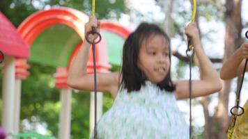 Cute sisters are having fun playing on the swings in a playground in a park. Children playing in the playground during summer vacation. video