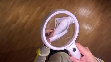 pov First person view man using magnifying glass for examining one hundred dollar bill, verifying authenticity and details on wooden table background video