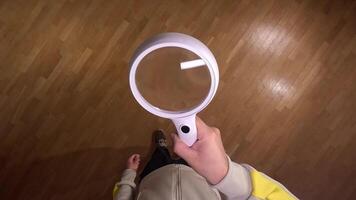 Curious person examines wooden floor with magnifying glass, searching for clues in intricate patterns and textures. Search for clues, detailed study, close examination, finding solution concept. video