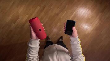 pov First person view Man effortlessly connects red wireless speaker to smartphone via bluetooth for music enjoyment in cozy indoor setting. Innovations enhance modern living video