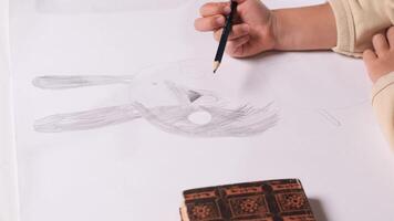 Close-up view of a young artist sketching a bunny rabbit face with a pencil on white paper. The focus highlights the creativity and concentration involved in the drawing process video