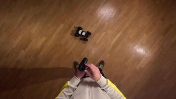 Person holding a remote control while playing with a radio controlled car on a parquet floor, seen from a first-person perspective. A man throws a radio-controlled car on the floor and is ready video