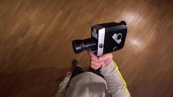 pov First person view Cameraman holding a vintage movie camera is recording on a parquet floor, offering a unique perspective from the operator's point of view video