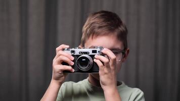 clode-up portrait little Boy learning photography is using an old rangefinder camera, carefully adjusting focus and framing the shot against a gray backdrop. Boy Take a picture with vintage old camera video