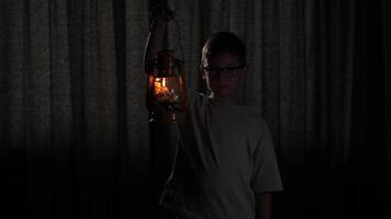 portrait of boy with lit old kerosene lantern lamp in dark room. Old lantern illuminates dark room. Curious boy in dark room with old vintage lantern in hand. boy with glasses peering into darkness video