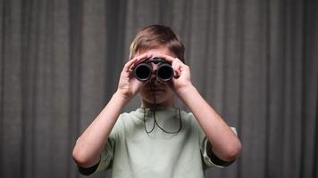 boy looking through binoculars. portrait of boy with binoculars. child peering into distance. concept of close examination. schoolboy looking through binoculars, looking into camera video