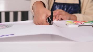 close-up of scissors cutting paper. little girl young artist focuses on cutting a sheet of paper with scissors. Careful movements showcase creativity and skill in a fun, engaging activity video