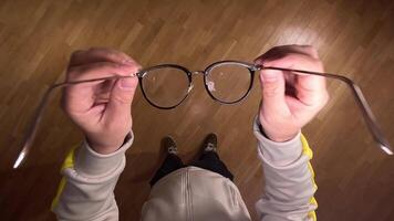 pov First person view Man putting on glasses. concept of deteriorating vision. Man casually holds stylish eyeglasses over a clean wooden floor, examining frames and lenses for clear vision video