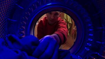 pov Young man pulling clothes out of washing machine in bathroom. View from inside washing machine. Young man is retrieving laundry from a front-loading washing machine video