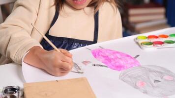 close-up of a child drawing with a brush and paint on a white sheet of paper.A little girl enthusiastically draws a rabbit with a paintbrush. A child dips a brush in water and paint for drawing video