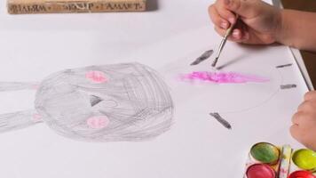 close-up of a child paints draws with a brush and paint on a white sheet of paper. A little girl paints a rabbit with a brush for painting video