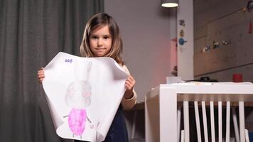 portrait of a Little girl is holding a piece of paper with a rabbit on it. Smiling brightly, girl showcases her artistic talent and creativity in a warm, inviting space video