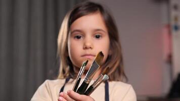 portrait of a little girl with brushes for painting. The child shows a set of brushes for painting. Preparation for a drawing lesson. Little girl at home paints with paints, watercolors video