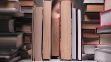 pequeno menina leva uma livro a partir de uma estante. menina leva uma livro dentro a biblioteca. cheio estante. menina escolheu uma livro em uma estante de livros video