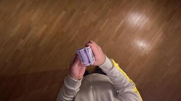 POV first person view Man standing on wooden floor, counting thick stack of hundred dollar bills, evoking wealth, success, and financial stability video