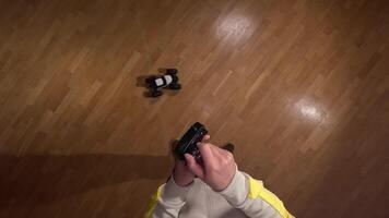 First-person view of a person holding a remote control and maneuvering a radio-controlled car across a polished wooden floor, creating a dynamic scene of indoor entertainment video