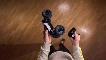 pov Person is holding a radio-controlled car and its remote control, standing on a wooden floor, preparing for a thrilling race or playful maneuver video