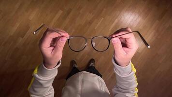 pov First person view Man casually holds stylish eyeglasses in a cozy home, showcasing trendy eyewear and clear vision importance. concept of deteriorating vision. Putting on glasses for vision video