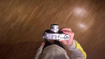 pov First person view Photographer is holding a vintage rangefinder camera above a wooden parquet floor, getting ready to take a picture from an overhead perspective video