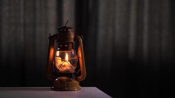 Old, burning kerosene lamp standing on white table illuminating dark room with out-of-focus curtains in the background, creating cozy and nostalgic atmosphere video