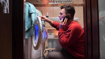 Homeowner experiencing laundry problems is making a phone call to an appliance repair service, gesturing in frustration at his broken washing machine video
