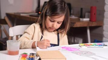 Young girl concentrating on painting a rabbit with watercolors at a white desk. The creative process unfolds in a peaceful home environment, showcasing her artistic talent and focus video
