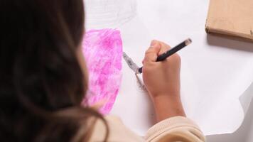 top view little girl Young artist carefully adding details to a colorful cartoon character drawing with a pink marker showcases creativity and imagination in a joyful. close-up video