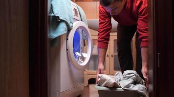 Man opening the door of a washing machine, preparing to load or unload laundry in a laundry room, with a basket of clothes nearby video
