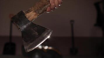 close up of man holding old axe. Lumberjack raises an axe in a dimly lit workshop. Shovels and various tools hang on the wall, creating a rustic atmosphere filled with craftsmanship and manual labor video