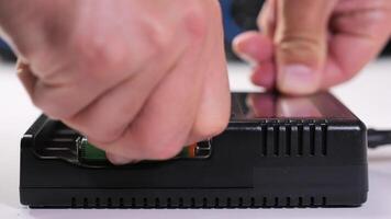 Technician loading four green cylindrical rechargeable batteries into a black charger featuring a digital display, showcasing precision and efficiency in an indoor workspace video