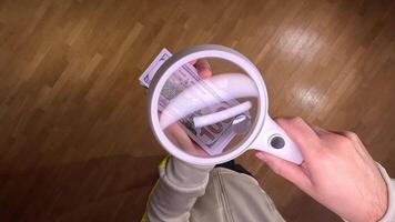 pov First person view Hands inspecting 100 usd bill with magnifying glass on wooden floor, emphasizing authenticity and scrutiny in finance video