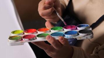 de cerca de un niño con un cepillo cosecha arriba pintar para cuadro. un conjunto de multicolor pinturas para pintura con un cepillar. para niños dibujo video