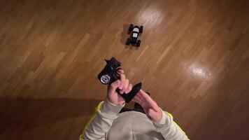 pov Hands holding a remote control and maneuvering a small remote control car on a parquet floor, offering a first-person perspective of indoor playtime video