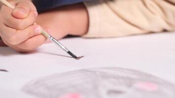 close-up of a child drawing with a brush and paint on a white sheet of paper. A little girl paints a drawing with a sieve for drawing video