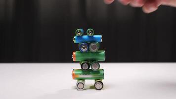 Person builds a colorful tower of batteries on a white surface, carefully stacking them until the structure collapses, creating a chaotic display of scattered batteries video