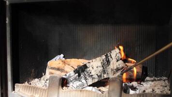 2631close-up of firewood in a fireplace. a man stirs burning logs in a fireplace. Person arranges a burning log in a fireplace using a poker. Flames dance as the log shifts, creating a warm and cozy video