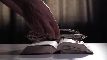 Priest places a crown of thorns on a holy bible, creating a poignant scene. A dark background contrasts with the illuminated bible, highlighting the significance of the moment video