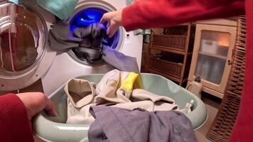 pov persona cargas ropa dentro un Lavado máquina en un bien organizado lavandería habitación a hogar, con estantería y detergente botellas azul ligero ilumina el escena. ocupado ama de casa cargando ropa video
