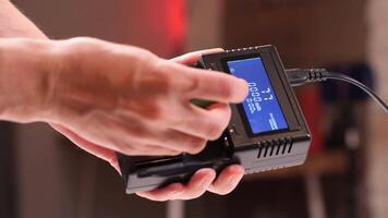 Close-up of a technician preparing a professional battery charger with a digital display, inserting four batteries one by one video