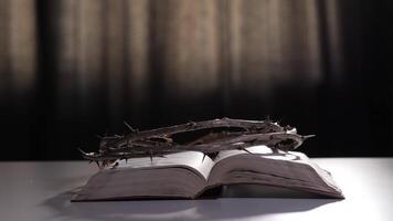 Crown of thorns rests on an open holy bible placed on a white table, contrasting against a dark background. The scene evokes themes of faith, sacrifice, and spirituality video