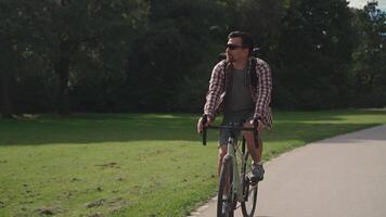 Handsome hipster with backpack and shirt enjoys a bicycle ride through a city park in summer sunny weather. A man riding a city cycle in Germany on a bicycle road. A guy on gravel bicycle in Munich. video