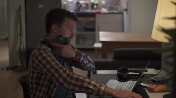 Cervical neck ache, nerve arthritis. Man studying late through night at laptop computer with cervical pain. Exhausted guy relaxing his neck using gun massager while overworking at notebook computer. video