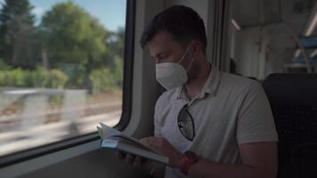 Passenger on public transport is reading a book while sitting by window wearing a protective mask. A man traveling on a Deutsche Trains wearing a protective mask and reading a book. German railroad. video