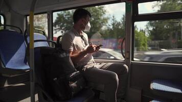 Passenger in ffp2 mask is on bus in Munich, browsing the Internet on mobile phone. Coronovirus regulations in Germany. Personal hygiene. Man on public transport using mobile app. Travel safely video