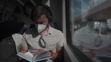 Passenger traveling on Deutsche train in summer with wireless headphones and reading book. Student reads study workbook with wireless earphones while commuting on train. Daily commute to university. video