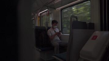 Masked man travels on train by window on summer day in sunny weather and uses smartphone. Man traveler in a mask rides a commuter suburban railway in Germany while surfing the Internet on his phone. video