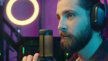 Positive Caucasian man blogger vlogger male in headphones speaker stream talk microphone device radio broadcast gamer smiling guy addict streamer play virtual game cyber sport online at home blog vlog video