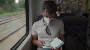 Passenger on public transport is reading a book while sitting by window wearing a protective mask. A man traveling on a Deutsche Trains wearing a protective mask and reading a book. German railroad. video