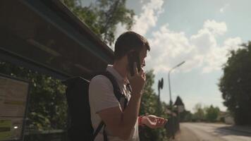Man checks time on wristwatch while waiting for bus at stop, calls to warn of delayed appointment, male communicates on cell phone while delaying tranport in Germany. An irritated male is late. video